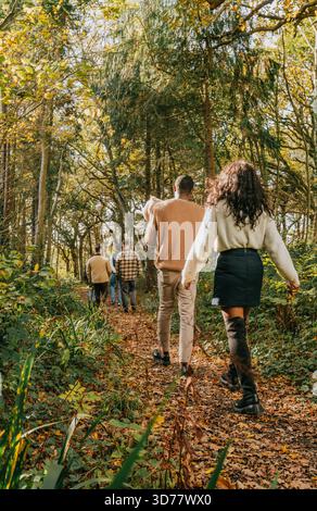 Eine Gruppe von Menschen läuft durch einen Wald, mit einer Frau, die einen Rock trägt. Die Szene ist friedlich und ruhig, während die Gruppe ihre gemeinsame Zeit genießt Stockfoto