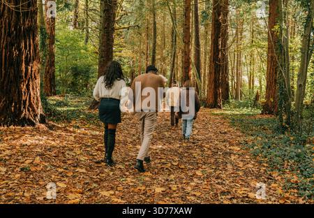 Eine Gruppe von Menschen läuft durch einen Wald, einige tragen Jacken. Die Szene ist friedlich und ruhig, während die Gruppe ihre Zeit genießt Stockfoto