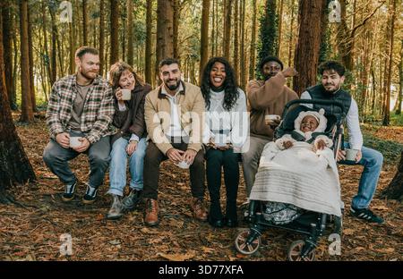 Eine Gruppe von Leuten, die in einem Wald sitzen, einige mit Bechern. Die Szene ist entspannt und freundlich Stockfoto