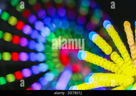 Dynamische Spirale aus bunten Bokeh-Lichtern, die bei Nacht aufgenommen wurden, bilden einen lebendigen, vom Festival inspirierten abstrakten Hintergrund, der ideal für kreatives Design ist. Stockfoto