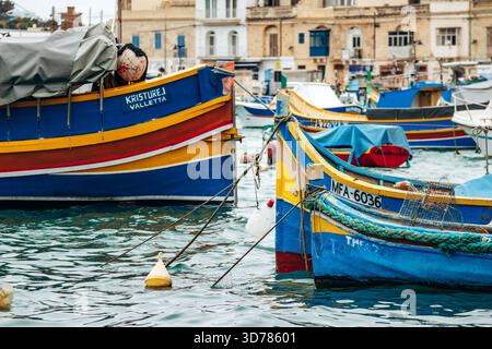 Marsaxlokk, Malta - 13. April 2025: Traditionelle, farbenfrohe maltesische Fischerboote namens Luzzu mit hellblauen, gelben und roten Details, die im malerischen Hafen von Marsaxlokk ankern Stockfoto