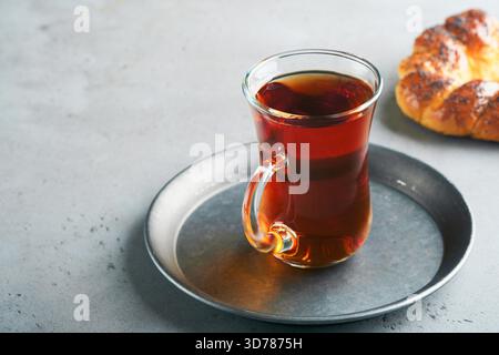 Türkischer schwarzer Tee. Eine Glasschale türkischer schwarzer Tee und knuspriger türkischer traditioneller Bagel auf grauem Betontischhintergrund. Frühstücksgebäck-Konzept. Traditionelles türkisches Heißgetränk. Stockfoto