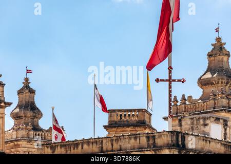 Flaggen, darunter die Flagge des Souveränen Malteserordens, die maltesische Nationalflagge, die Vatikanische Flagge und andere auf dem historischen Gebäude im Zentrum von Birgu. Stockfoto