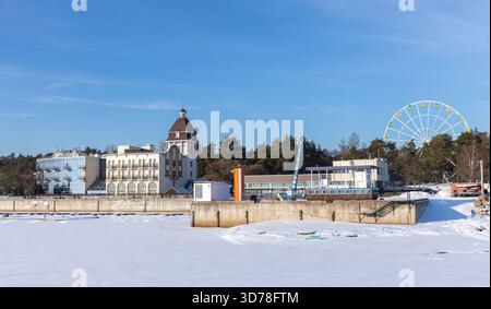 Terijoki Country Club, seitliches Foto an einem sonnigen Wintertag, Zelenogorsk, Russland. Eine ruhige Winterlandschaft am Wasser bietet ein großes Riesenrad Stockfoto