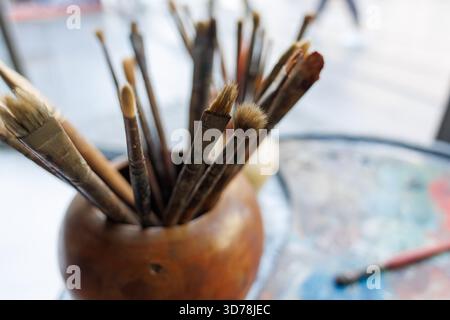 Pinselkollektion des Künstlers in einem Holzhalter auf einem farbenfrohen Tisch in einem kreativen Arbeitsbereich Stockfoto