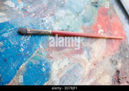 Malpalette mit Pinsel, der auf leuchtenden Farben im Atelier eines Künstlers aufliegt Stockfoto