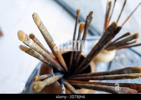 Pinselkollektion des Künstlers in einem Holzhalter auf einem farbenfrohen Tisch in einem kreativen Arbeitsbereich Stockfoto