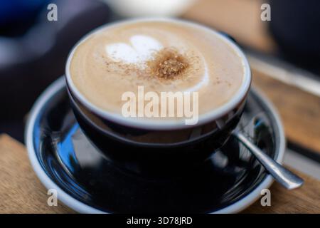 Cremiger Latte in einer schwarzen Tasse mit Zimt bestreut in einem gemütlichen Café während der Morgenstunden Stockfoto