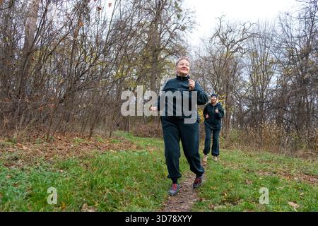Alte Seniorinnen, die im Herbst auf dem Trail joggen. Sportliche Aktivitäten für alte Menschen. Glückliche Frau, die draußen läuft Stockfoto