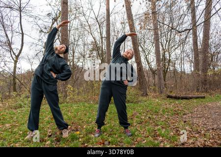 Seniorin, die mit Personal Trainer Outdoor trainiert. Stretching mit Sportlehrer. Stockfoto