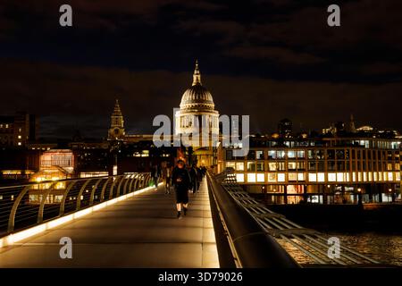 Ein nächtlicher Blick auf die Menschen, die über die Millennium Bridge über die Themse mit einer beleuchteten Kuppel der St. Pauls Cathedral im Hintergrund spazieren. Stockfoto
