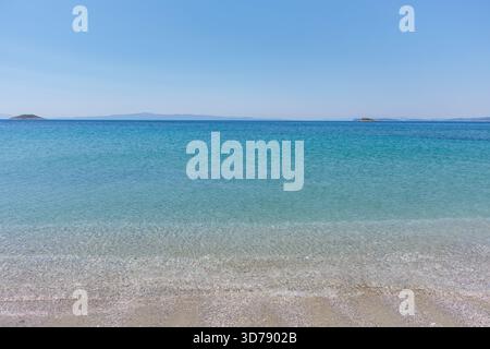 Sanfte Wellen schlagen gegen einen Sandstrand unter klarem Himmel und enthüllen kristallklares Wasser Stockfoto