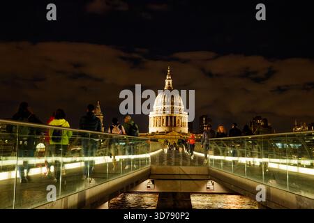 Die Leute laufen nachts über die Millennium Bridge mit der beleuchteten Kuppel von St. Pauls im Hintergrund, London, England. Stockfoto
