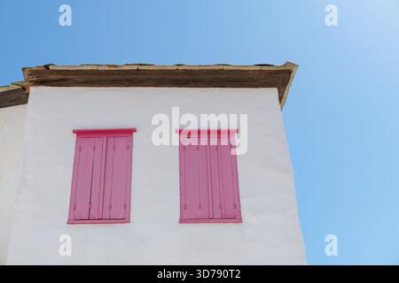 Weißes Gebäude mit pinkfarbenen Holzläden vor blauem Himmel Stockfoto