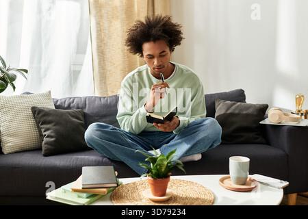 Ein nachdenklicher junger Mann genießt einen ruhigen Moment zu Hause, schreibt und entspannt sich in seinem gemütlichen Raum. Stockfoto