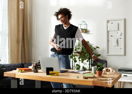 Ein stilvoller junger Mann steht an seinem Schreibtisch, entspannt und lächelnd in seinem einladenden Arbeitsplatz. Stockfoto