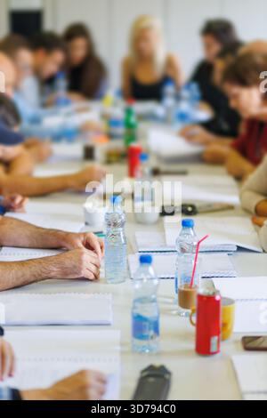 Gemeinsame Brainstorming-Sitzung an einem großen Tisch mit Teilnehmern, die an einem modernen Arbeitsplatz diskutieren und Notizen machen Stockfoto