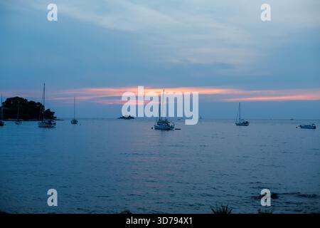 Wunderschöne Dämmerung über einer ruhigen Bucht mit Segelbooten, die bei Sonnenuntergang im ruhigen Wasser ankern Stockfoto