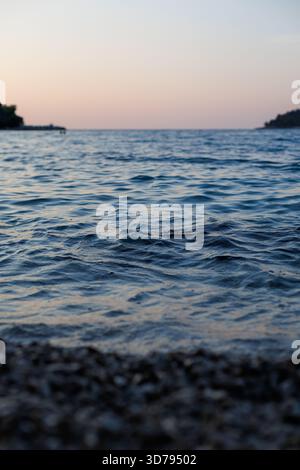 Ruhiger Abend am Wasser, während die Wellen in der Abenddämmerung sanft gegen das Ufer schlagen Stockfoto