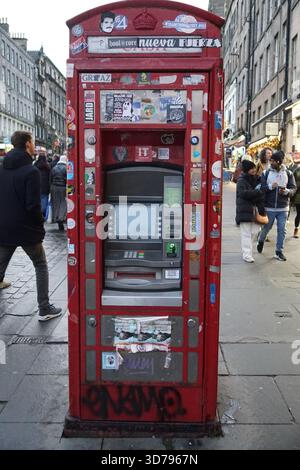 Eine rote britische Telefonbox, die in einen Geldautomaten umgewandelt wurde, mit Aufklebern bedeckt, auf einer belebten Straße in Edinburgh. Edinburgh, Schottland Stockfoto