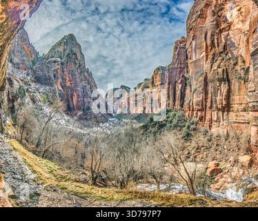 Winterschluchtszene im Zion-Nationalpark mit Sandsteinklippen, Fluss und schneebedecktem Gelände. Stockfoto