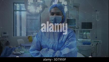 Stehende Chirurgin in blauem Kleid und Maske, Arme im Operationssaal mit digitalem Netz kreuzen Stockfoto