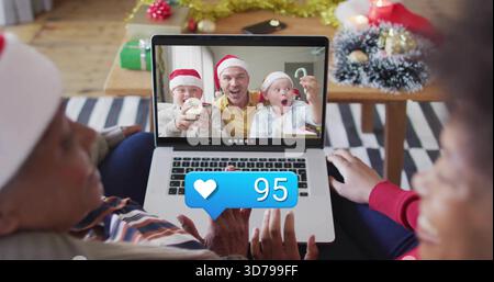 Beobachten Sie Familienmitglieder, die Anrufe auf einem Laptop zu Hause mit Santa Hats und Herzbenachrichtigung 95 sehen Stockfoto