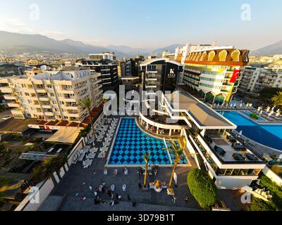 Alanya, Türkei - 13. Juni 2024: Blick aus einem hohen Winkel auf den Kaila Beach Hotel Komplex und seinen Poolbereich, umgeben von Wohnhäusern mit Bergen Stockfoto