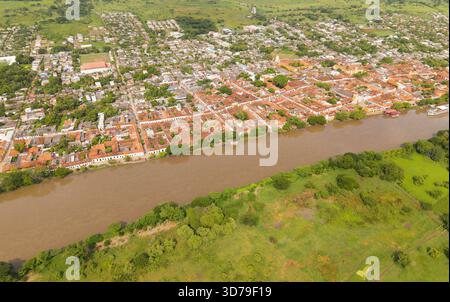 Aus der Vogelperspektive treffen die Terrakotta-Dächer auf den schlammigen Flussrand, im Kontrast zur lebhaften grünen Landschaft Mompox, Santander, Kolumbien. Stockfoto