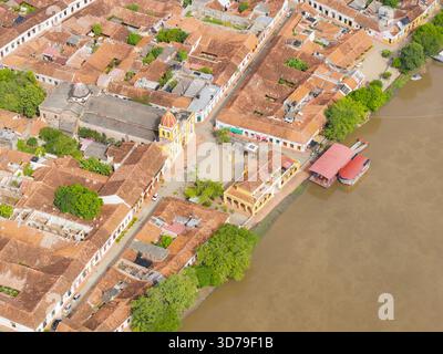 Aus der Vogelperspektive treffen die Terrakotta-Dächer auf den schlammigen Rand des Flusses magdalena, eingerahmt von der hellen Fassade der Kirche und dem lebhaften Grün der Bäume Mompo Stockfoto
