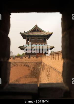 Blick auf alte braune Backsteinmauern, die einen traditionellen chinesischen Turm mit einem gestuften grünen Dach vor einem weichen Himmel umgeben, Jinzhong, Shanxi, China. Stockfoto