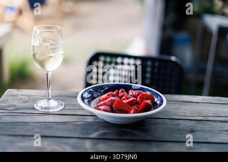 Genießen Sie frische Erdbeeren und Weißwein auf einem rustikalen Holztisch in entspannter Atmosphäre im Freien Stockfoto