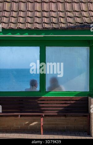 Silhouette eines Paares, das in einem alten Schutzhaus am Strand oder am Meer in Shanklin an der Küste der isle of wight UK sitzt Stockfoto