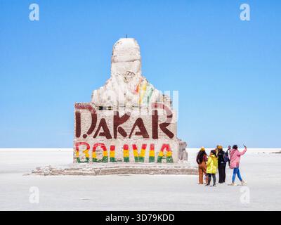 Touristen am Dakar-Denkmal, eine Skulptur aus Salz, die eine gekleidete Figur auf den Uyuni-Salzflächen in Bolivien zum Gedenken an die Rallye Dakar darstellt Stockfoto
