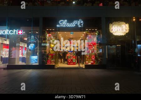 Der Lindt-Laden in Liverpool, EINER nachts. Das Schaufenster ist zu Weihnachten mit roten und goldenen Verpackungen dekoriert und zeigt Schokolade. Stockfoto