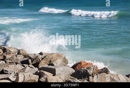 Wellen in türkisfarbenem Wasser erreichen das Ufer und brechen gegen die Felsen. Stockfoto