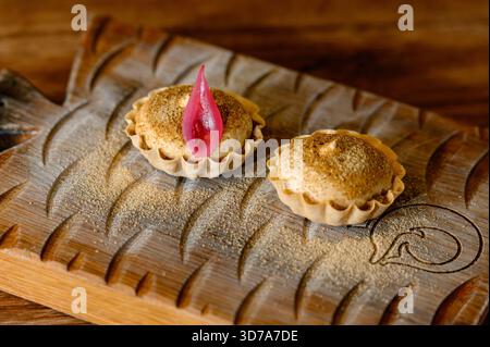 Zwei Törtchen mit Pastete und Gewürzen werden auf einem geschnitzten Holzbrett serviert. Kulinarische Präsentation von Mini-Kuchen auf einem handgemachten Brett in einem Restaurant Stockfoto