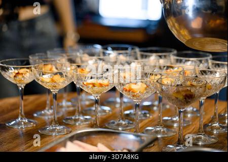 Verschiedene Kristallgläser mit Früchten auf einem hölzernen Banketttisch. Individuelle Desserts in Gläsern mit Pfirsichen für Gäste an der Rezeption. Stockfoto