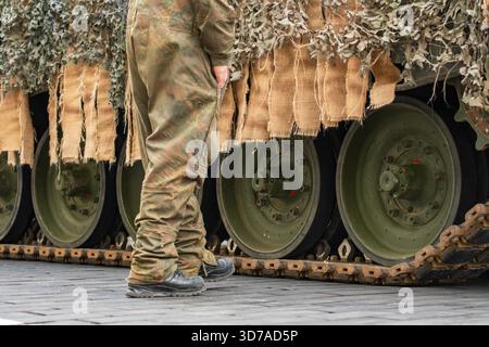 Soldat in militärischer Tarnung in der Nähe eines Panzerpanzers Leopard, der auf der Straße unterwegs ist Stockfoto