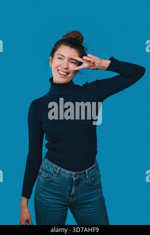 Lässige Frau mit Friedenszeichen, glückliches weibliches Model mit lässiger Kleidung und freundlichem Verhalten Stockfoto