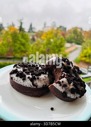 Verführerische Schokoladen-Donuts mit reichhaltigem Keksen- und Creme-Topping. Zwei glasierte Gebäckstücke werden auf einen weichen Fokus gesetzt Stockfoto