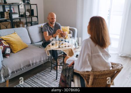 Entspanntes Paar trinkt Tee gemütliches Wohnzimmer, das warme Gespräche teilt und einen ruhigen Morgenmoment genießt. Die gemütliche Atmosphäre zu Hause betont die Verbindung Stockfoto