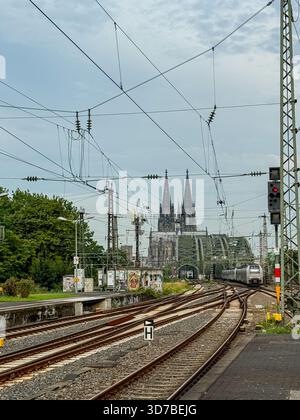 Bahngleise, die bei Sonnenaufgang bei bewölktem Himmel in Köln zur Hohenzollernbrücke und zum Dom führen Stockfoto