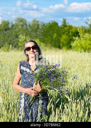 Attraktive Seniorin mit Blumenstrauß im Weizenfeld Stockfoto