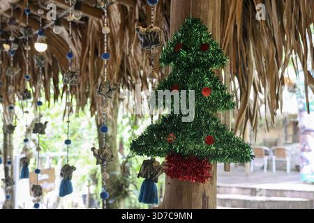 Festliches grünes Lametta weihnachtsbaumschmuck hängt draußen von Holzpfosten. Dieses fröhliche Weihnachtsschmuck bringt Urlaubsstimmung in die tropische rus Stockfoto