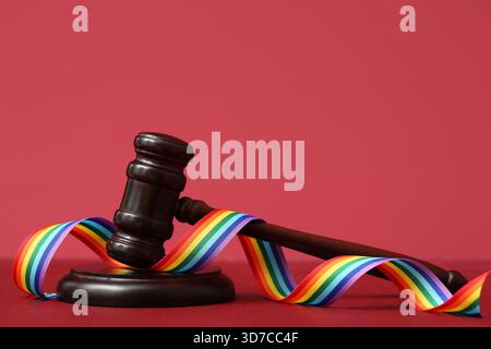 Richterlicher Hammer mit Regenbogenband auf rotem Tisch. LGBT-Konzept Stockfoto