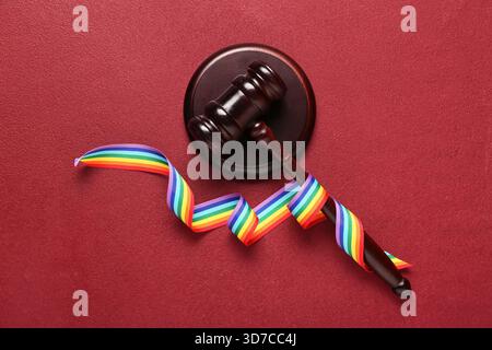 Richterlicher Hammer mit Regenbogenband auf rotem Hintergrund. LGBT-Konzept Stockfoto