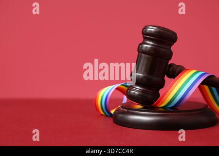 Richtergabel mit Regenbogenband auf rotem Tisch, Nahaufnahme. LGBT-Konzept Stockfoto