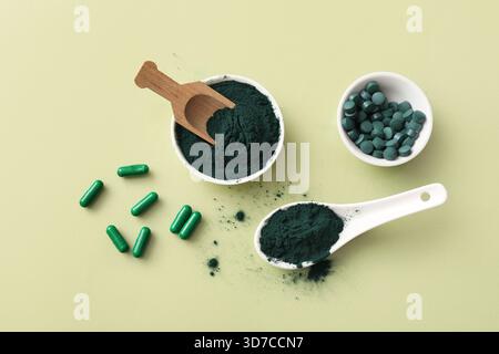 Schüsseln mit Spirulina-Pulver und Tabletten mit Holzlöffel auf grünem Hintergrund Stockfoto
