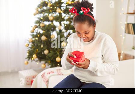 Frohe Weihnachten und frohe Neujahrsfeiertage afroamerikanerin, die Geschenkbox öffnet Stockfoto